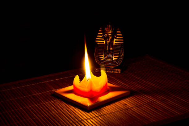Statue of Tutankhamun lit by a candle on bamboo mat on a black background.