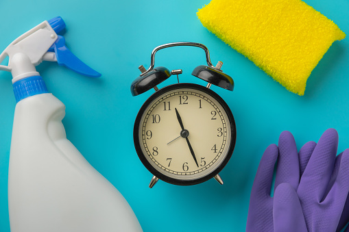 Cleaning time with cleaning materials and tools. clock and cleaning products on a blue background