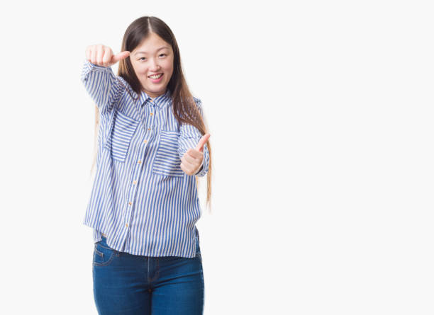istock Young Chinese woman over isolated background approving doing positive gesture with hand, thumbs up smiling and happy for success. Looking at the camera, winner gesture. 1069221708