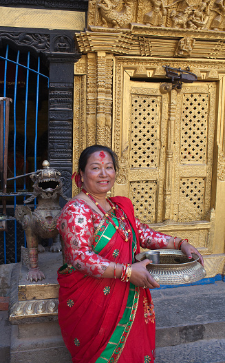 Bhaktapur, Nepal - January 23, 2017: Smiling Newari woman in red sari poses for a photo in Hindu temple on Durbar square