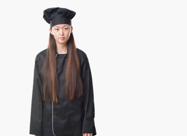 istock Young Chinese woman over isolated background wearing chef uniform with serious expression on face. Simple and natural looking at the camera. 1069228730
