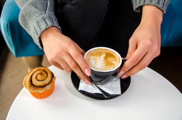 istock woman hand holding espresso coffee and cinnamon roll 1069230876