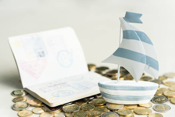 Traveling, holiday, summer and vacation  concept. Mini sailboat and passport on pile of coins. stock photo