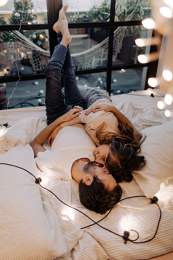 Photo of young couple in the morning, lying in bedroom in their apartment during Christmas holidays