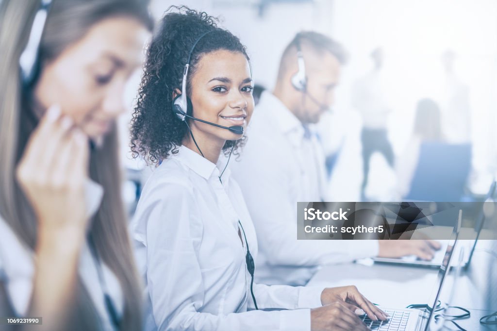 Call center worker accompanied by her team. Call center worker accompanied by her team. Smiling customer support operator at work. Young employee working with a headset. Call Center Stock Photo