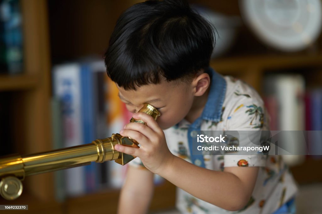 kid or boy concentrates telescope indoors Child Stock Photo