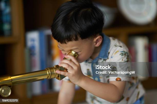 Kid Or Boy Concentrates Telescope Indoors Stock Photo - Download Image Now - Child, Lens - Optical Instrument, Telescope