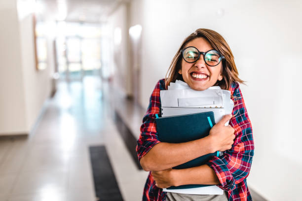 Happy nerdy student with books in a school hallway. Young nerdy student holding books and papers with her eyes closed in a school hallway. nerd teenager stock pictures, royalty-free photos & images