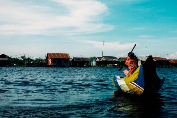 mulher local atravessando o lago em sua canoa em frente o assentamento de casa flutuante palafitas - flood people asia cambodia - fotografias e filmes do acervo