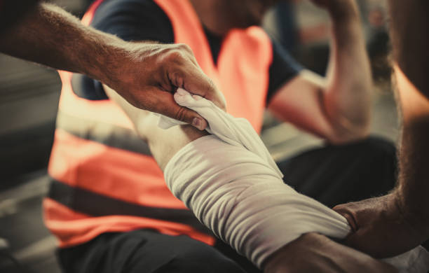 Taking care of physical injury at work! Close up of unrecognizable manual worker assisting his colleague with physical injury in a warehouse. bandage photos stock pictures, royalty-free photos & images