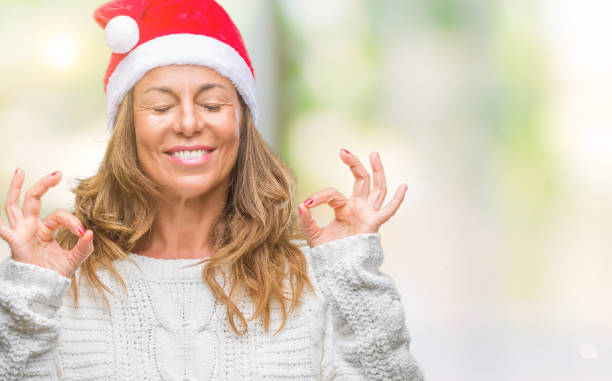 moyen age senior femme hispanique usure noël chapeau sur fond isolé se détendre et sourire avec les yeux fermés faisant le geste de la méditation avec les doigts. concept de yoga. - holiday emotional stress christmas santa claus photos et images de collection