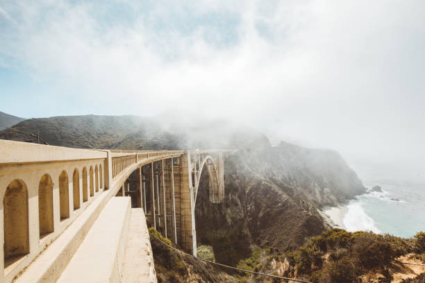 Panoramic view of historic Bixby Creek Bridge along world famous Highway 1 on a sunny day with fog in summer, Monterey County, California, USA