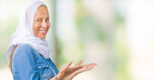 istock Middle age eastern arab woman wearing arabian hijab over isolated background Inviting to enter smiling natural with open hand 1069254746