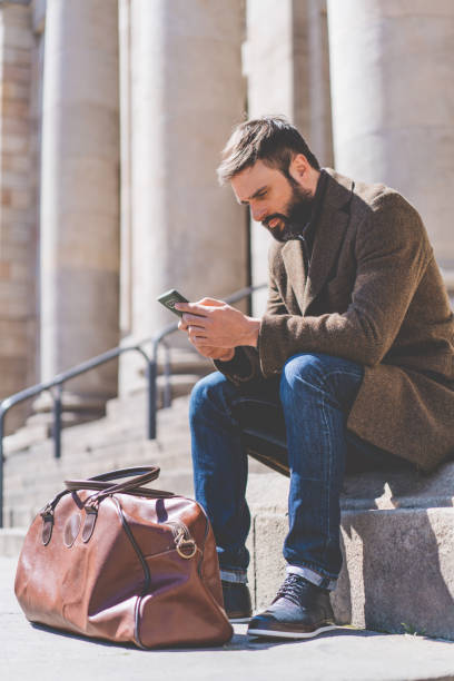 istock Adult Bearded Man using smartphone outside. Casual professional entrepreneur texting message on smartphone outside old building.Vertical. 1069258004