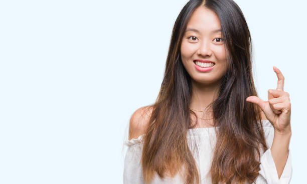 istock Young asian woman over isolated background smiling and confident gesturing with hand doing size sign with fingers while looking and the camera. Measure concept. 1069260550