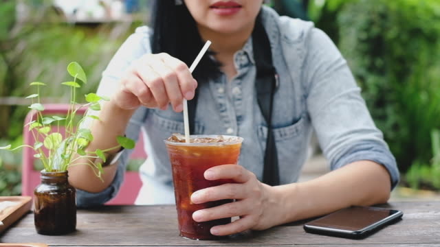 slow motion asian woman stirring ice tea at coffee shop in sunny day.summer drink
