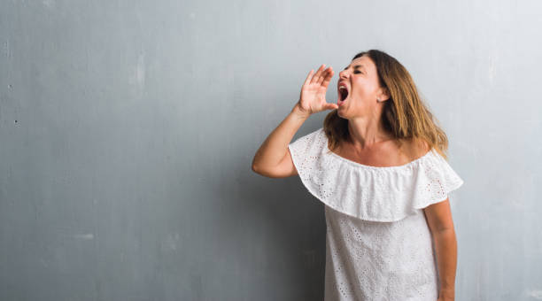 istock Middle age hispanic woman standing over grey grunge wall shouting and screaming loud to side with hand on mouth. Communication concept. 1069265100