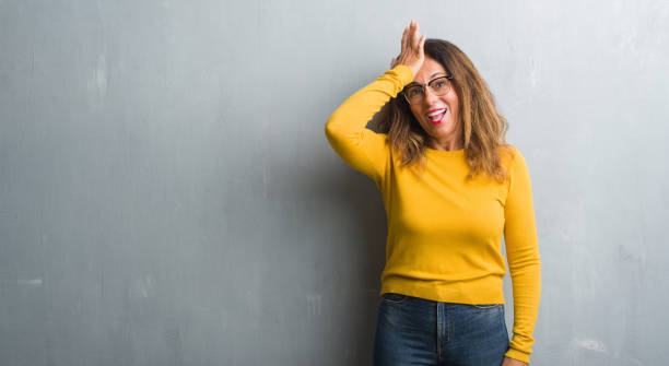 istock Middle age hispanic woman over grey wall wearing glasses surprised with hand on head for mistake, remember error. Forgot, bad memory concept. 1069265224