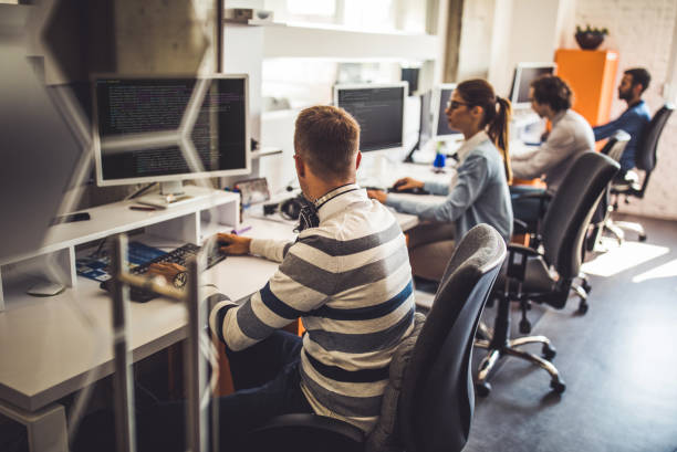 Group of computer programmers working on PC's in the office. Group of programmers developing new software on desktop PC's in the office. Focus is on man in the foreground. worker working stock pictures, royalty-free photos & images