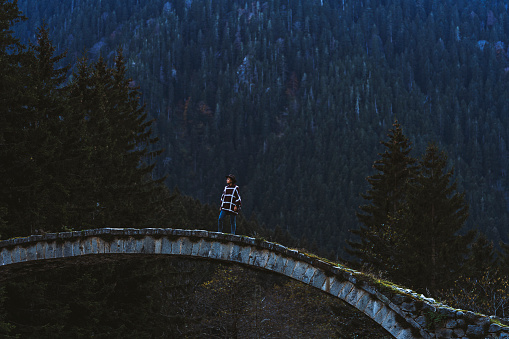 Young woman crossing the stone bridge over river near mountainside, Çilanç Bridge, Rize