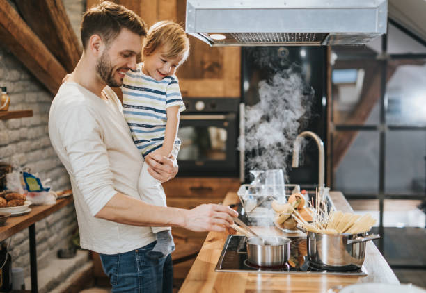 Happy father holding his small boy while cooking lunch in the kitchen.