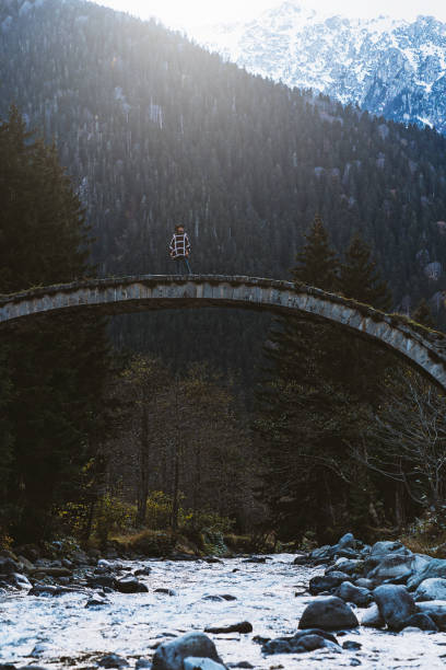 Young woman crossing the stone bridge over river near mountainside, Çilanç Bridge, Rize