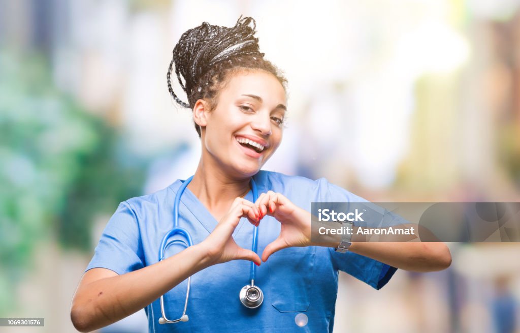 Young braided hair african american girl professional surgeon over isolated background smiling in love showing heart symbol and shape with hands. Romantic concept. Nurse Stock Photo