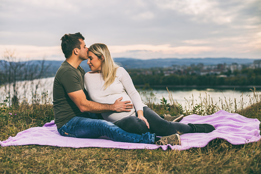 Happy husband kissing his pregnant wife into forehead and enjoy spending time together outdoor.Toned image.