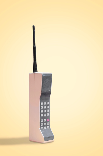 Obsolete retro mobile cellular phone on a vintage yellow background on a vertical image with copy space and room for text