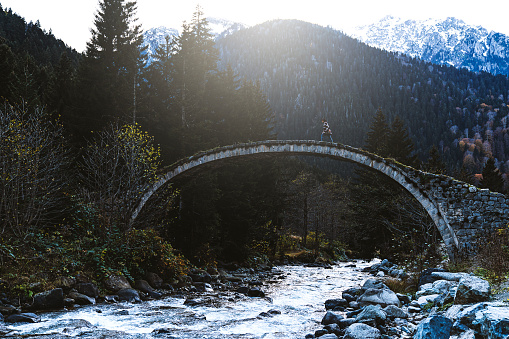 Young woman crossing the stone bridge over river near mountainside, Çilanç Bridge, Rize