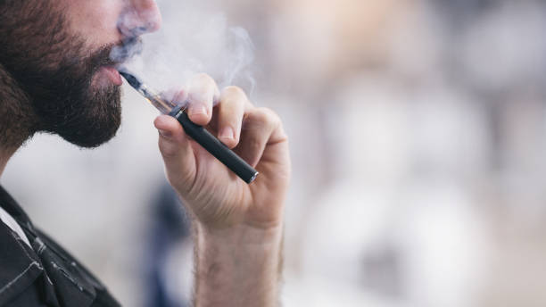 Young male worker smoking electronic cigarette Smoking electronic cigarette. Shallow DOF. Developed from RAW; retouched with special care and attention; Small amount of grain added for best final impression. 16 bit Adobe RGB color profile. electronic cigarette stock pictures, royalty-free photos & images