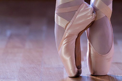Close-Up of Woman feet, dressing a pair of pointe shoes on a parquet floor of a dance school