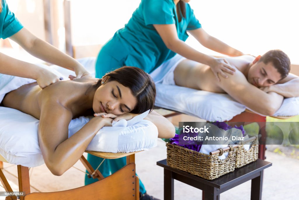 Lovers Feeling Peaceful During Wellness Therapy Honeymoon couple relaxing while getting body massage from masseuses at dayspa Spa Stock Photo