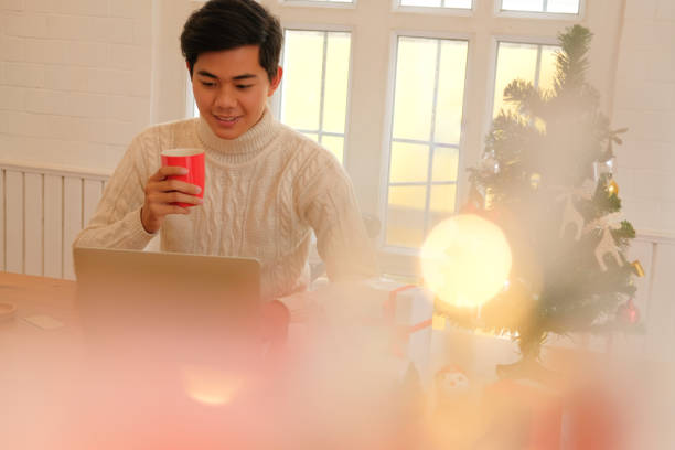 istock man holding coffee cup & using computer at home during christmas. xmas new year celebration 1069364564