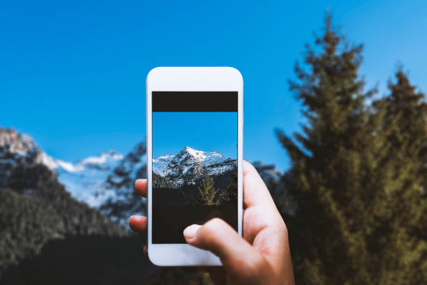 Hand holding smart phone, photographing scenic snowy mountain view