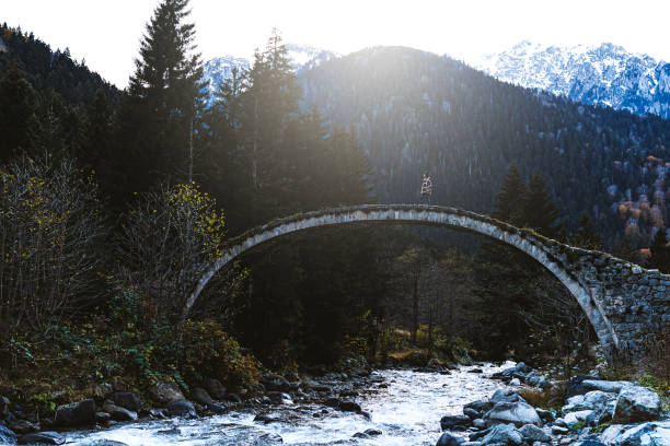 Young woman crossing the stone bridge over river near mountainside, Çilanç Bridge, Rize