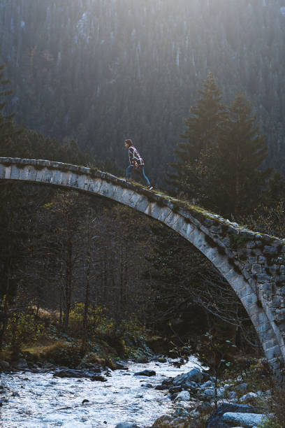 Young woman crossing the stone bridge over river near mountainside, Çilanç Bridge, Rize