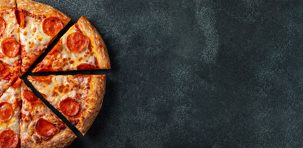 Tasty pepperoni pizza and cooking ingredients tomatoes basil on black concrete background. Top view of hot pepperoni pizza. With copy space for text. Flat lay. Banner.