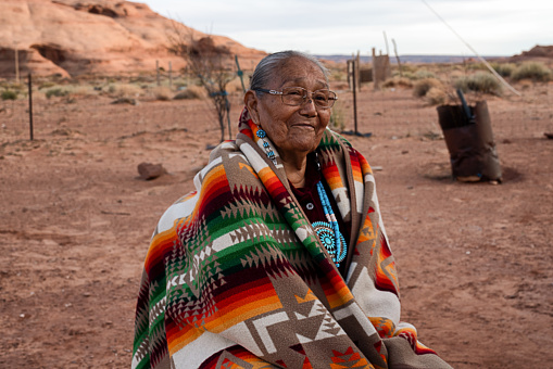 Happy and cheerful 85-year-old Native American Navajo grandmother posing for a portrait on a dirt yard in Monument Valley Arizona