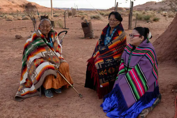 Three generation women, with two grandmothers and a granddaughter, all native American Navajo women sitting and posing in a group outside