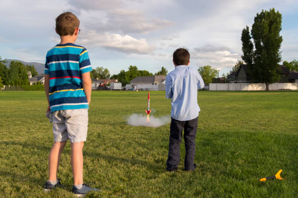 Model Rocket Launching Boys These two boys are launching a model rocket in a large playground field.  This photo shows the moment of ignition as the rocket is pushing off from its platform trailing a flame and smoke. model rocket stock pictures, royalty-free photos & images