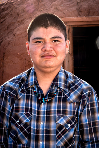 happy and cheerful teenage Navajo native american boy posing outside a traditional hogan