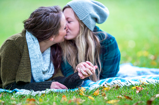 A couple are lying on a blanket in a meadow and kissing each other. They are a lesbian couple.