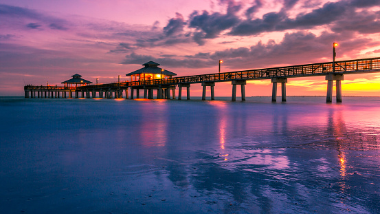 A colorful golden and purple sunset falls beneath the horizon at the Fort Myers Beach Pier in Florida, USA. Long exposure seascape background with copy space.