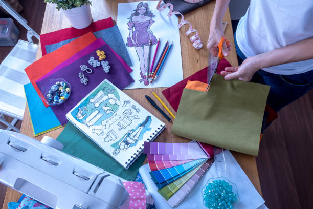 istock Fashion designer (tailoress) cutting fabric while working with drawing sketch, material & sewing machine at worktable 1069462886