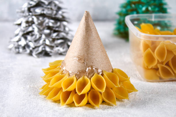 istock How to make a Christmas tree from raw pasta conchiglie. The process of making Christmas trees from pasta, cardboard plates, hot glue and paint or spray. Guide, step by step on the photo.Handmade, DIY. 1069470936