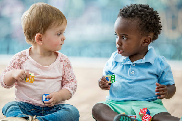 Infant friends Two infants are sitting and playing with toy blocks in a play room. They are looking at each other. baby boy stock pictures, royalty-free photos & images