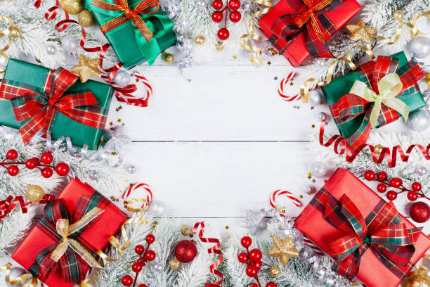 istock Gift or present boxes, snowy fir tree and christmas decorations on white wooden table top view. 1069478476