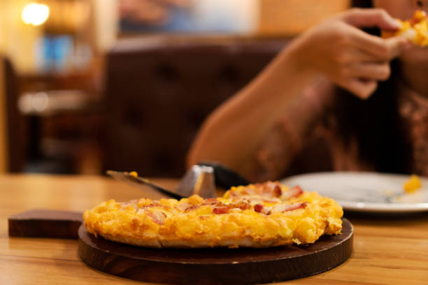 la giovane donna si diverte a mangiare la pizza hawaiana su un tavolo di legno con bevande analcoliche bianche nel ristorante. - human hand baked food pineapple foto e immagini stock