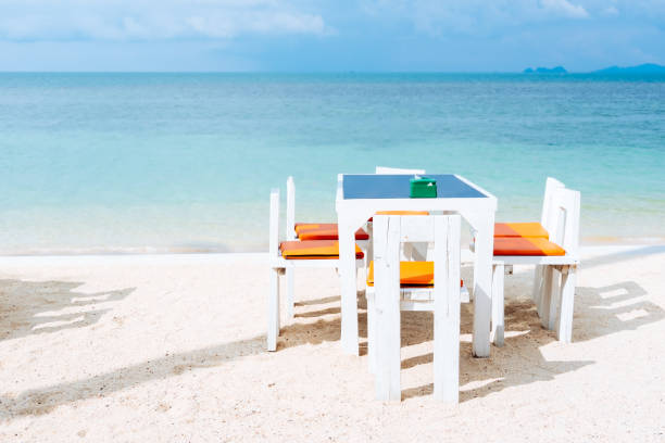 istock Outdoor white dinner table setting on white sand summer beach and calm blue sea background at restaurant or hotel. 1069481568